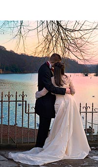 Romantic: bride and groom looking out across water at beautiful sunset.