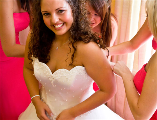 bride smiling as her wedding dress is laced up
