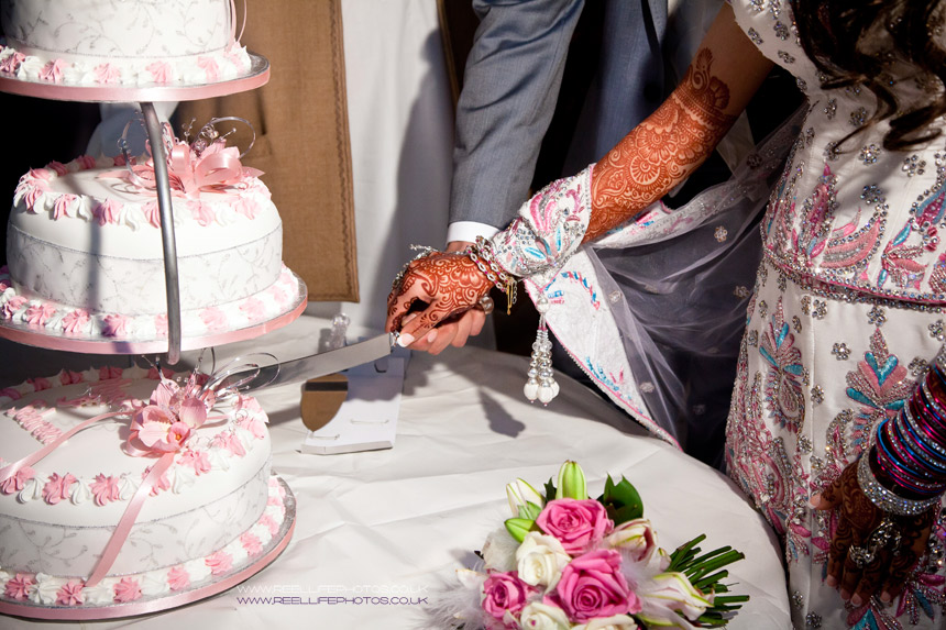 Asian bride and groom's hands as they cut their wedding cake